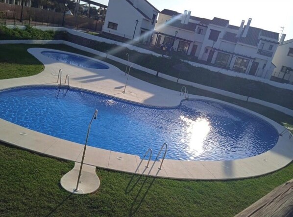 A swimming pool with a curved design, surrounded by a grassy area and a building in the background.