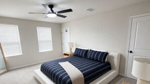 Quarto com cama, ventilador de teto, mesa de cabeceira, luminária e porta.