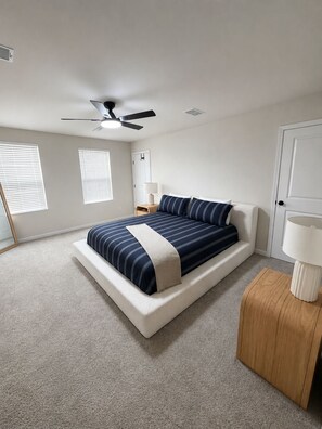 Ein Schlafzimmer mit einem Bett, einem Deckenventilator, einem Nachttisch, einer Lampe und einer Tür.