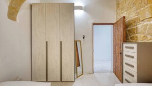 Ein Schlafzimmer mit Kleiderschrank, Spiegel, Bett und einer Steinwand.