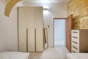 A bedroom with a wardrobe, a mirror, a bed, and a stone wall. - Stylish 2BR Maltese Maisonette w/ Terrace, Luqa (Ħal Luqa)