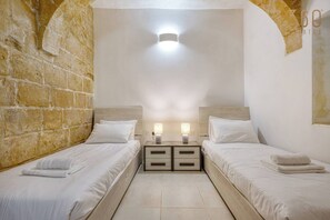 A hotel room with two beds, a nightstand with a lamp, and a stone wall. - Stylish 2BR Maltese Maisonette w/ Terrace, Luqa (Ħal Luqa)
