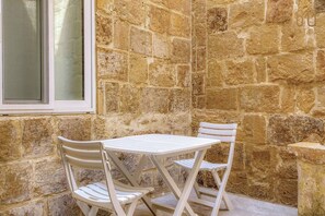 A corner with a stone wall, a window, and a white table with two chairs. - Stylish 2BR Maltese Maisonette w/ Terrace, Luqa (Ħal Luqa)