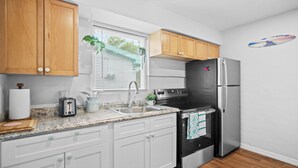 Una cocina con armarios de madera, un refrigerador de acero inoxidable, un horno negro, un lavaplatos y una ventana con persianas.