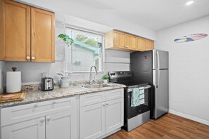 A kitchen with wooden cabinets, a stainless steel refrigerator, a black oven, a sink, and a window with blinds. - AC. Private 2-Unit property near the beach & 5th Ave South in Downtown Naples (Naples)