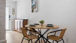 Un comedor con una mesa redonda, cuatro sillas de mimbre, una planta en maceta y un cuadro colgado en la pared.