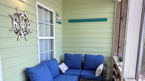 A covered porch with a blue sofa, wicker furniture, and a decorative wheel. - Drift Away, a Charming Coastal Cottage with pool and hot tub (Gulf Shores)