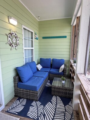 Eine überdachte Veranda mit einem blauen Sofa, Korbmöbeln und einem dekorativen Wagenrad.