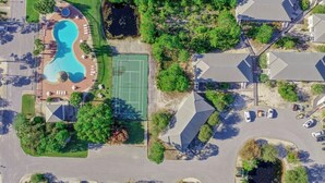 An aerial view of a residential area with a swimming pool, tennis court, and houses. - Drift Away, a Charming Coastal Cottage with pool and hot tub (Gulf Shores)