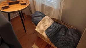 A cozy room with a round wooden table, a lamp, a wicker chair, and a small bed with a knitted blanket. - Drift Away, a Charming Coastal Cottage with pool and hot tub (Gulf Shores)
