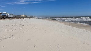 A beach with a clear sky, sandy shore, and a row of beach houses. - Drift Away, a Charming Coastal Cottage with pool and hot tub (Gulf Shores)
