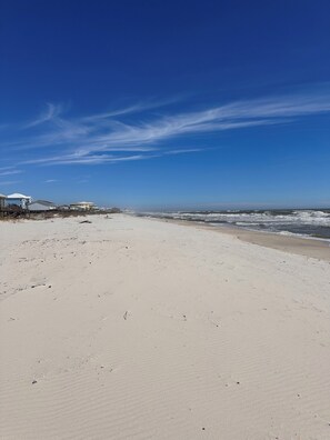 Ein Strand mit blauem Himmel, sandigem Ufer und einer Reihe Strandhäuser.