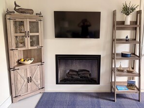 Ein Wohnzimmer mit Holzschrank, Kamin, Wandfernseher und Bücherregal.
