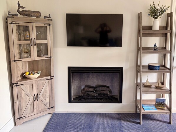 A living room with a wooden cabinet, a fireplace, a television mounted on the wall, and a bookshelf.