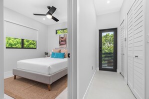 A bedroom with a bed, a ceiling fan, a window, a door, and a view of greenery outside. - LUXE 4BR Pool Oasis Near Wynwood & Design District (Miami)
