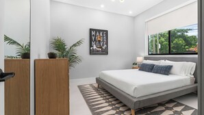 Ein modernes Schlafzimmer mit einem Bett, einem Wandbild, einem Fenster und einer Topfpflanze.