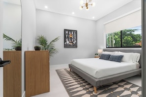 A modern bedroom with a bed, a wall-mounted picture, a window, and a potted plant. - LUXE 4BR Pool Oasis Near Wynwood & Design District (Miami)