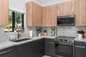Une cuisine moderne avec des meubles de couleur sombre, un four en acier inoxydable, un four à micro-ondes et un plan de travail en marbre.