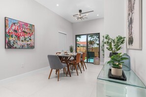 A dining area with a glass table, chairs, and a modern ceiling light fixture. - LUXE 4BR Pool Oasis Near Wynwood & Design District (Miami)