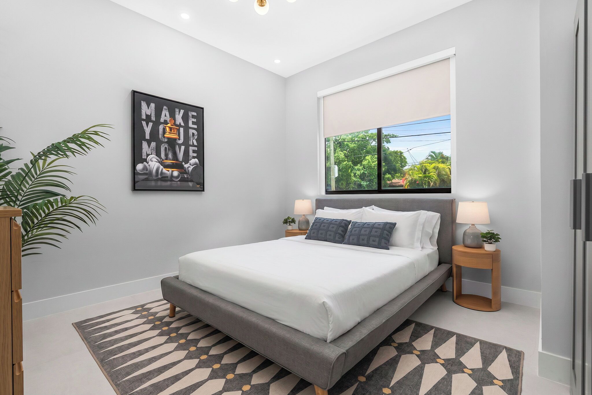 A modern bedroom with a large bed, a motivational poster, a window with a view, and a potted plant.