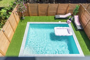 A rectangular swimming pool with a floating mat, surrounded by a wooden fence and artificial grass. - LUXE 4BR Pool Oasis Near Wynwood & Design District (Miami)