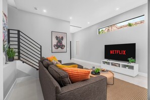 Un salon moderne avec un canapé gris, un téléviseur à écran plat et un escalier doté d’une rampe noire.