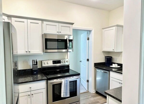 Cocina compacta con gabinetes blancos, microondas, estufa y cafetera.