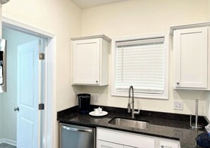 A kitchen with white cabinets, a black countertop, a stainless steel sink, and a window with blinds.