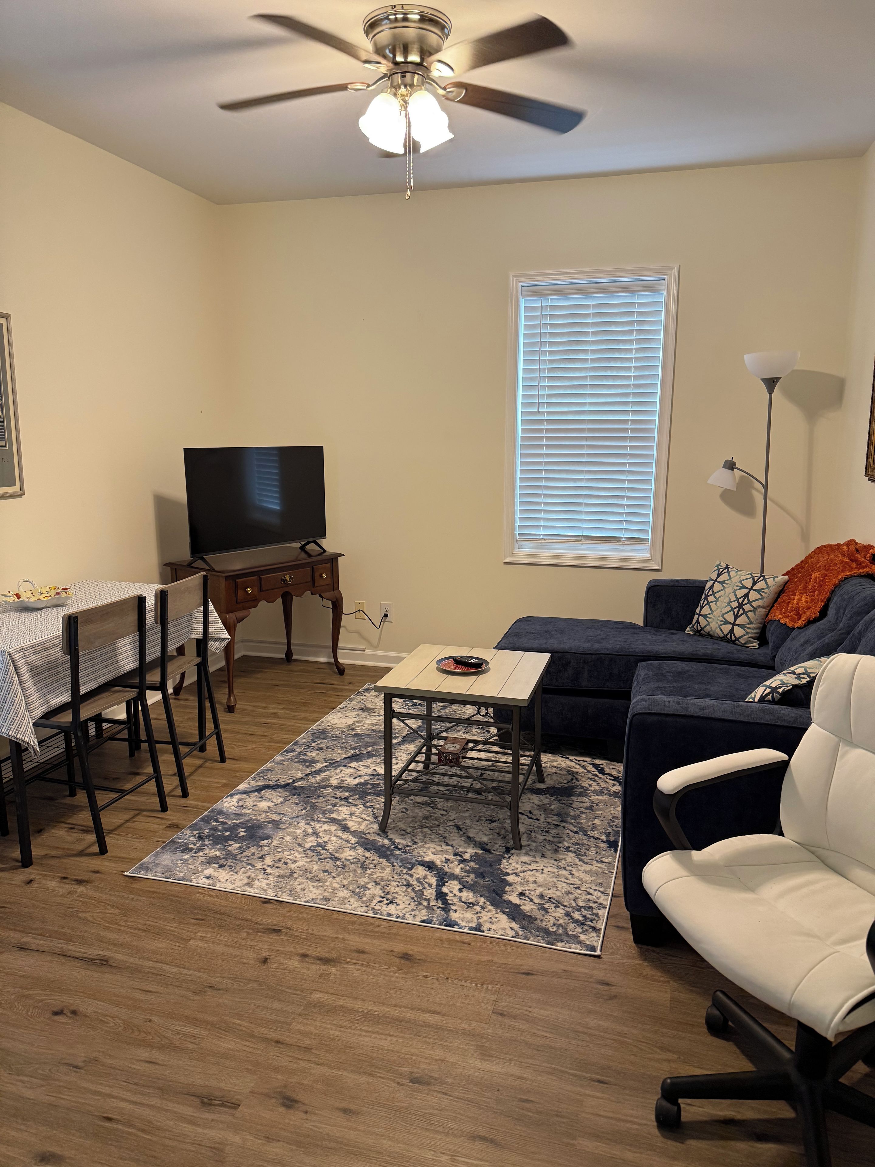 A living room with a ceiling fan, a television, a sofa, a coffee table, and a dining area with chairs and a table.