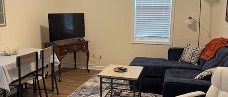 A living room with a ceiling fan, a television, a sofa, a coffee table, and a dining area with chairs and a table.