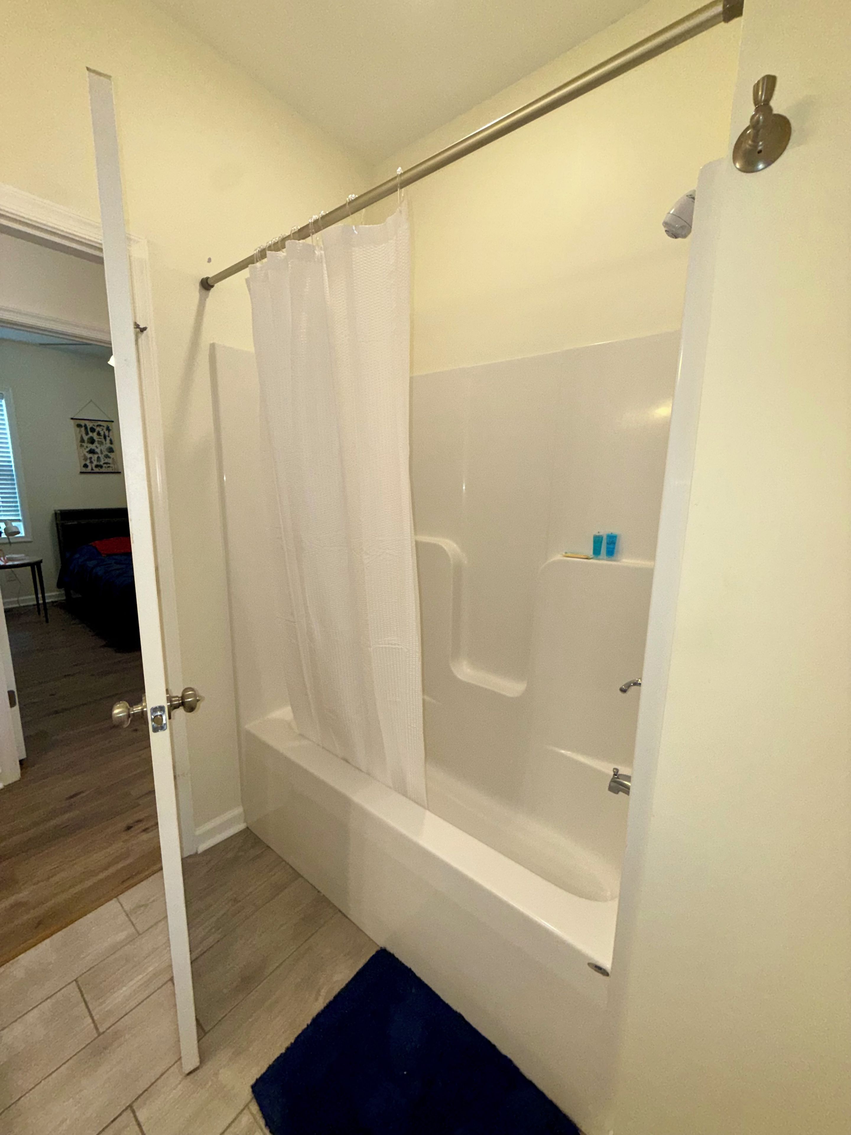 A bathroom with a bathtub, a shower curtain, and a door leading to another room.