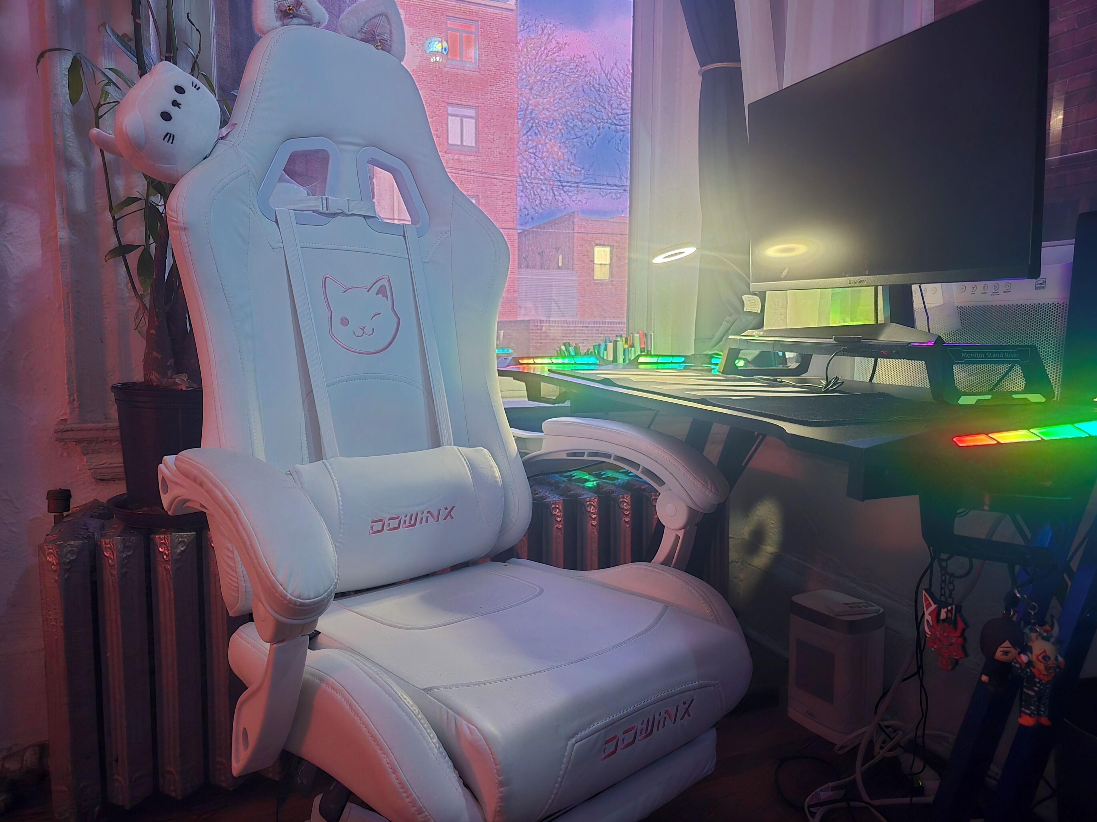 A gaming chair with a cat design, a monitor stand, and a desk with colorful LED lights.