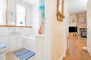 Ein modernes Badezimmer mit einer Badewanne, einem Waschbecken und einer Toilette. Ein Holzboden und ein gemustertes Teppich sind vorhanden.