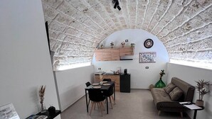 Een gezellige woonkamer met een gebogen plafond, een eethoek met een tafel en stoelen, een bank en een klein bijzettafeltje met een plant.