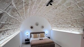 Een slaapkamer met een gewelfde plafond, een bed, nachtkastjes en wandlampen.