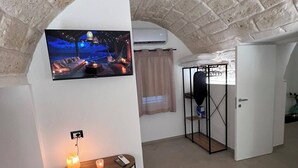 Een gewelfd plafond met een bakstenen patroon, een flatscreen televisie aan de muur bevestigd, een klein tafeltje met een kaars, en een deur die naar een andere kamer leidt.