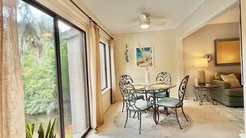 A spacious room with a dining area, large windows, and a ceiling fan.