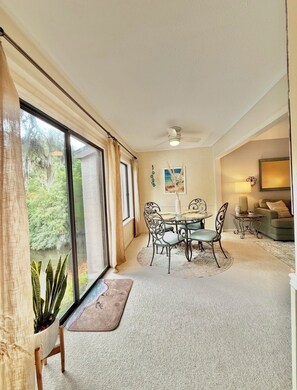 A spacious room with a dining area, large windows, and a ceiling fan.