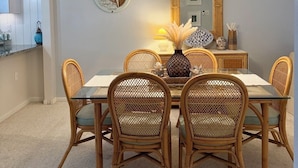 Un comedor con una mesa redonda, seis sillas de mimbre, un jarrón decorativo y un reloj montado en la pared.