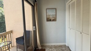Un balcón con puerta corredera de vidrio, una silla, una mesita, un tapete marrón y un cuadro en la pared.