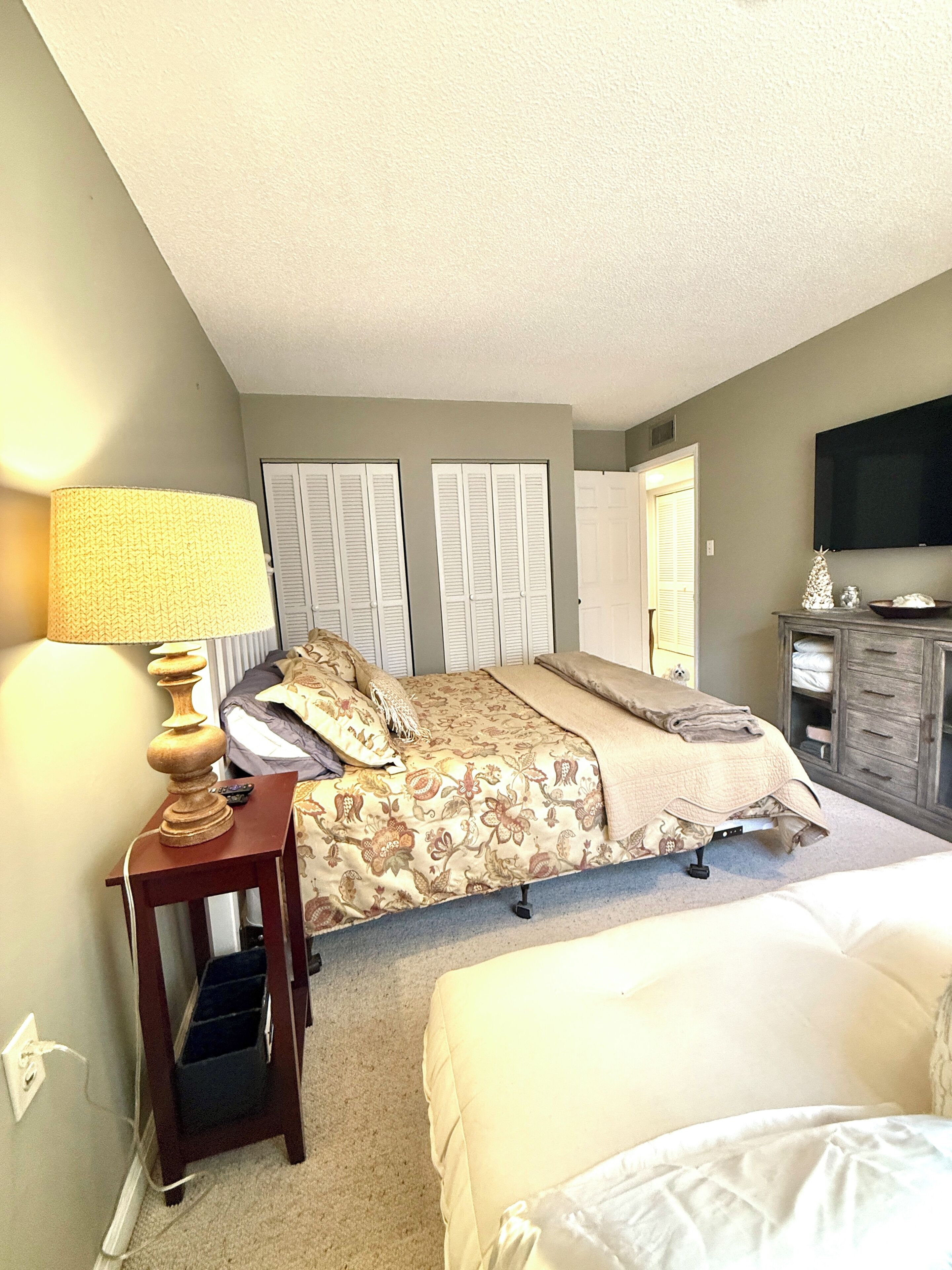 A bedroom with a bed, bedside table, lamp, wardrobe, and a television on the wall.