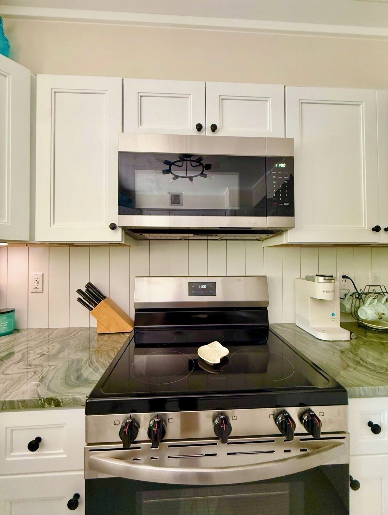 A kitchen with a stainless steel stove, a microwave above it, and white cabinets.