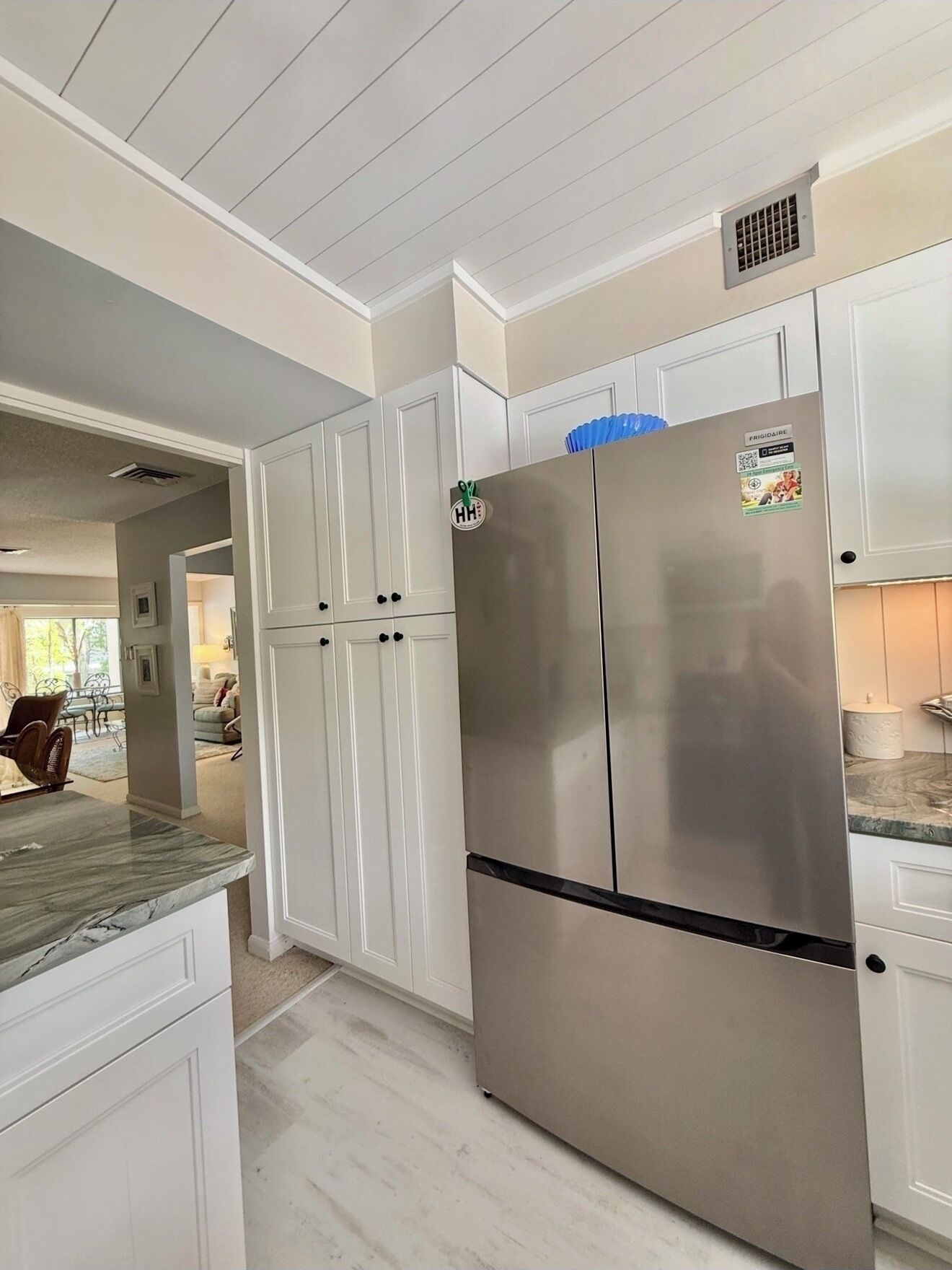 A kitchen with white cabinetry, a stainless steel refrigerator, and a marble countertop.