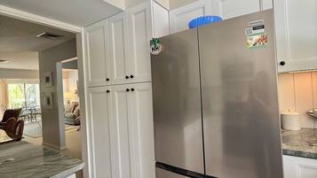 A kitchen with white cabinetry, a stainless steel refrigerator, and a marble countertop.