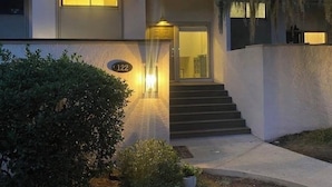 Un edificio con un cartel con el número 122, unas escaleras que llevan a una puerta y una entrada bien iluminada.