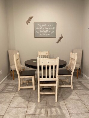 A dining area with a round table, four chairs, and a wall-mounted sign. - Family Fun Meets Cozy Comfort - 3 Bedrooms, 2 Bathrooms, Game Room and Hot Tub! (Odessa)