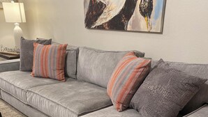 A grey sectional sofa with multiple pillows, a lamp, and a painting on the wall. - Family Fun Meets Cozy Comfort - 3 Bedrooms, 2 Bathrooms, Game Room and Hot Tub! (Odessa)