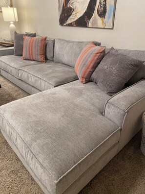 A grey sectional sofa with multiple pillows, a lamp, and a painting on the wall. - Family Fun Meets Cozy Comfort - 3 Bedrooms, 2 Bathrooms, Game Room and Hot Tub! (Odessa)