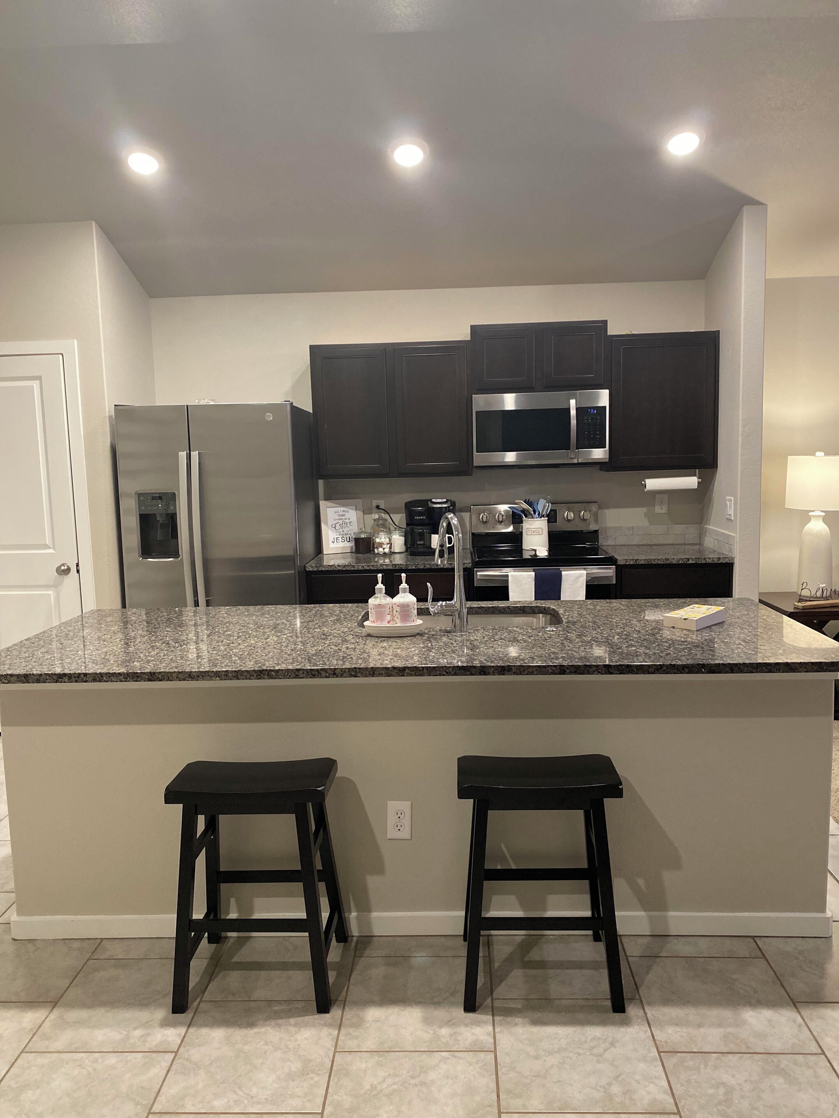 A kitchen with dark cabinets, stainless steel appliances, a granite countertop, and two bar stools.