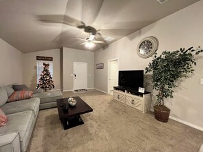 Uma sala de estar com ventoinha no teto, televisão em um móvel, árvore de Natal e planta em vaso.